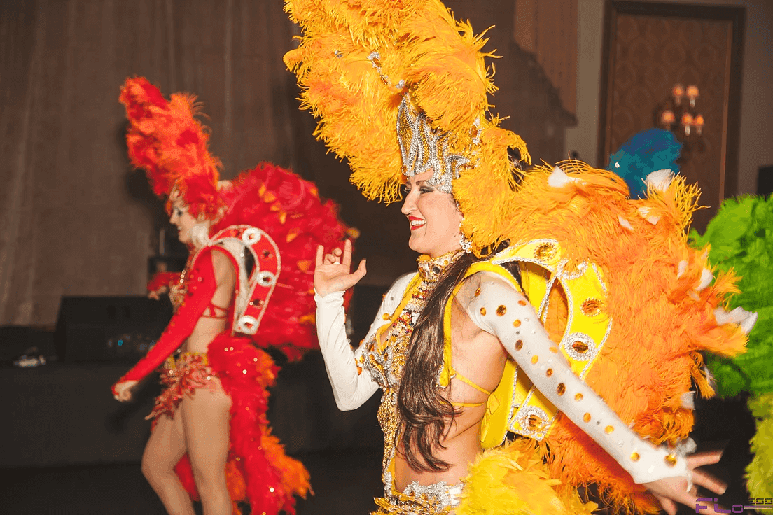 Samba dancers in orange and red feathered costumes performing at the gala