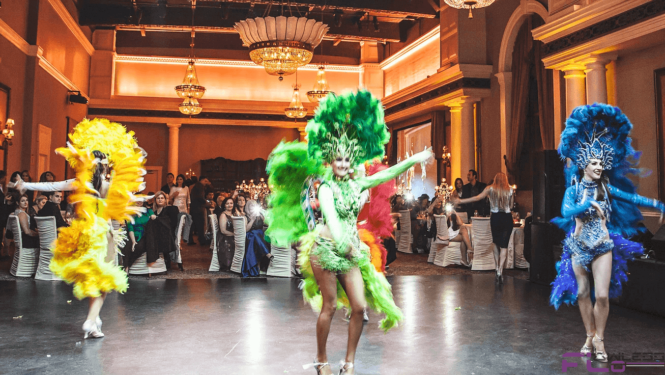 Carnival dancers in yellow, green and blue feathers perform in the chandeliered ballroom