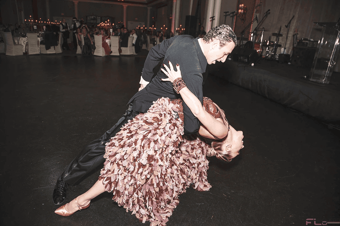 Ballroom dancer dipping his partner on the dance floor, band stage and guests behind