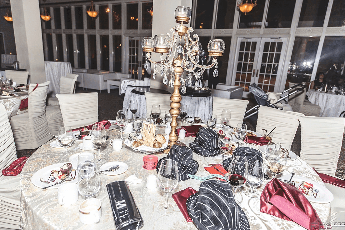 Dinner table with gold candelabra, burgundy napkins and striped fedora hats as favours
