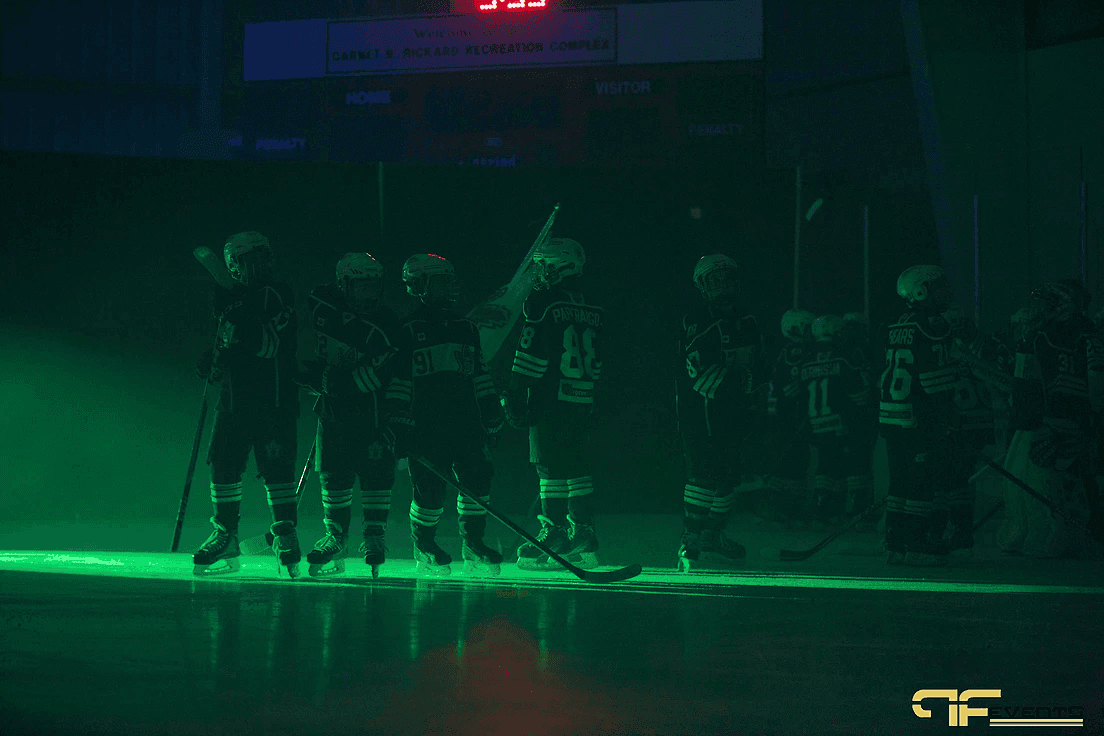 Team lined up on the ice bathed in green light under the arena scoreboard