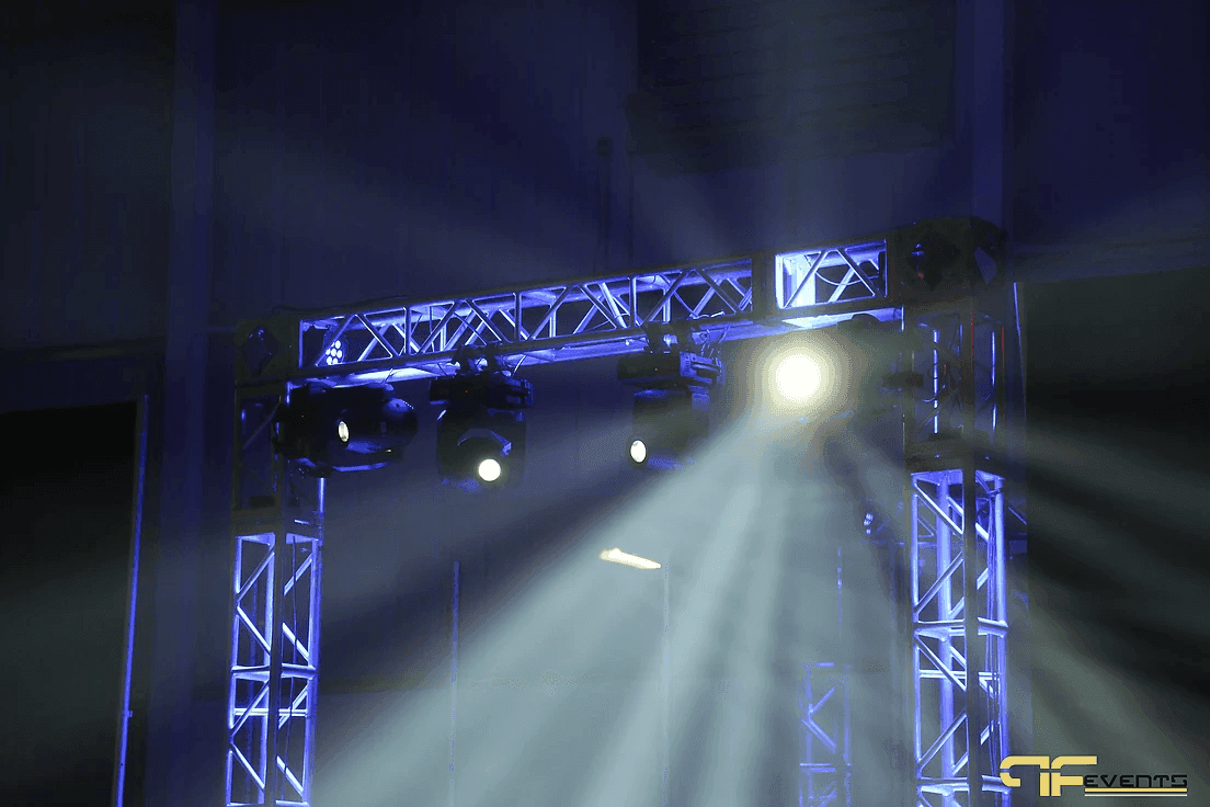Moving heads on the blue-lit truss arch cutting beams through haze