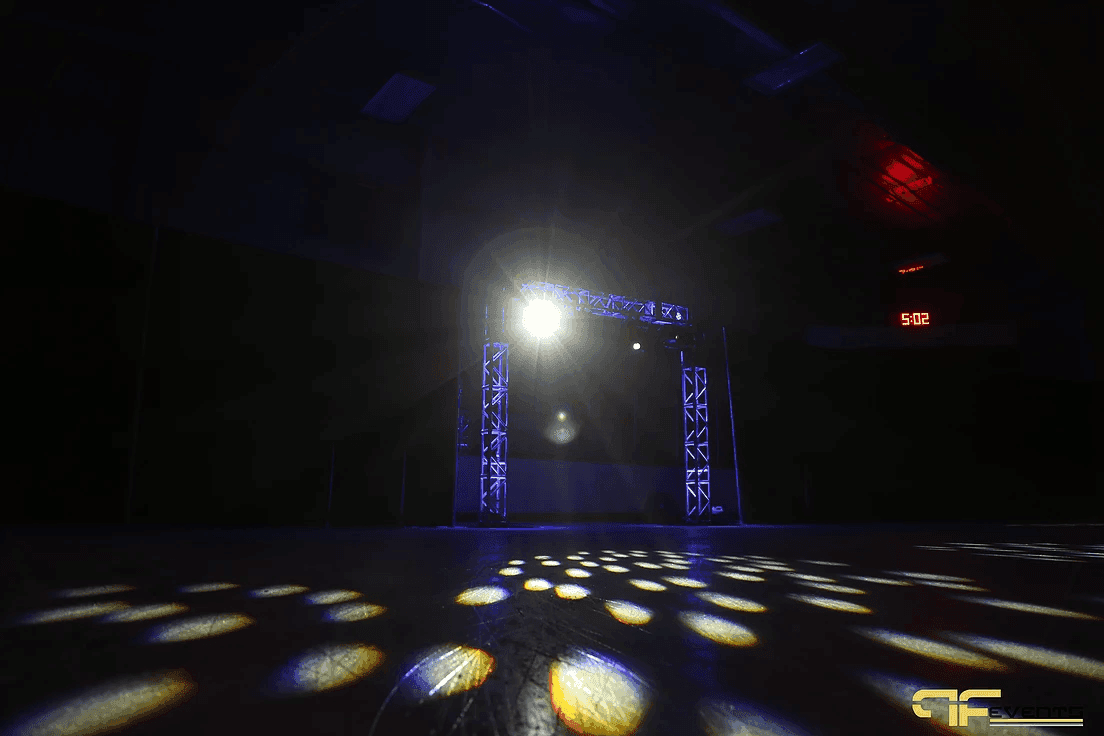Darkened arena with a bright beam from the truss arch and gobo spots across the ice