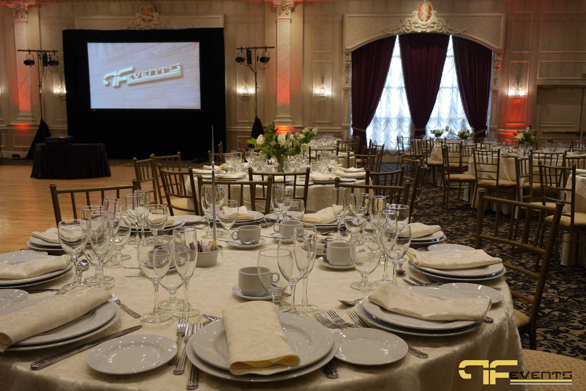 Ballroom at Château Le Jardin set with ivory linens, florals and a projection screen