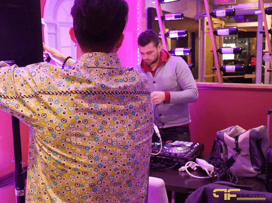 DJ at a controller beside a speaker stand in magenta light