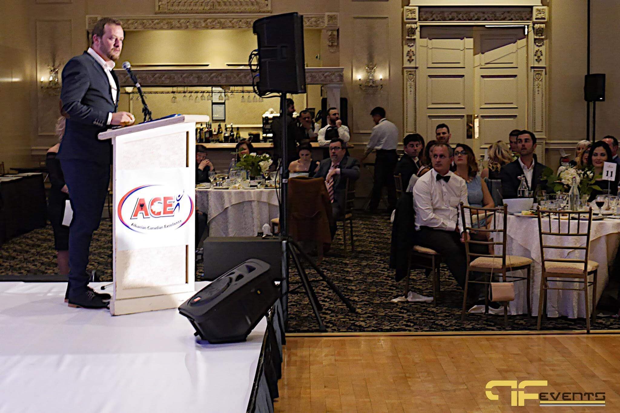 Speaker at an ACE-branded lectern with speakers on stands in the ballroom