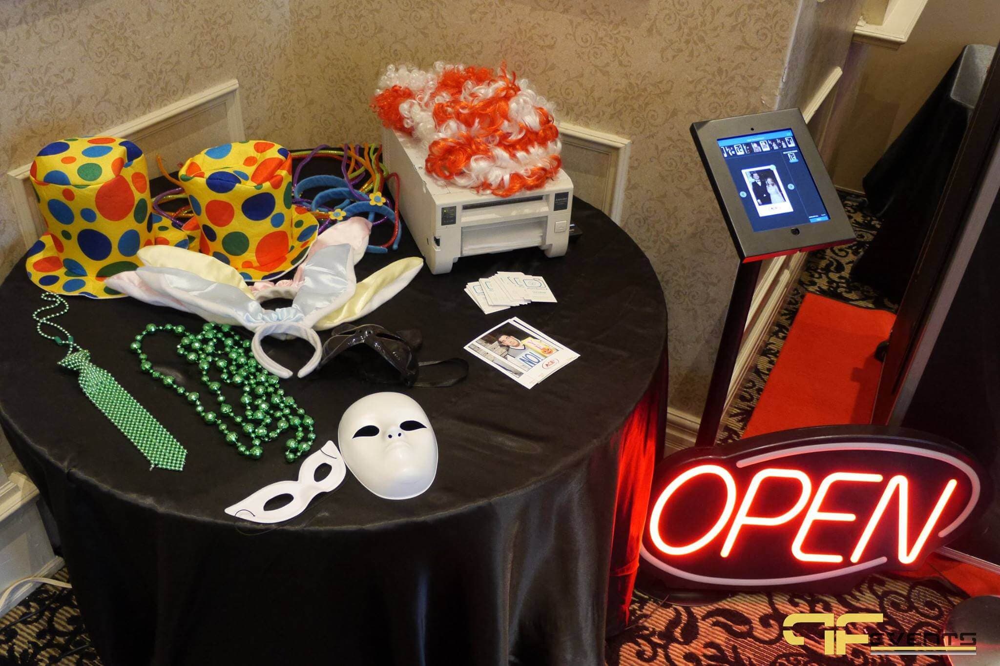 Photo booth props, printer and tablet kiosk beside a neon OPEN sign