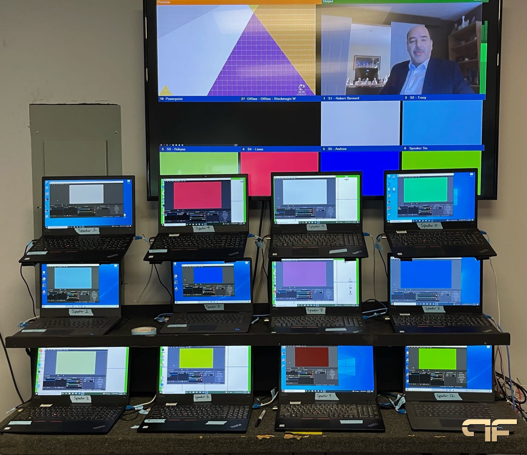 Wall of twelve labelled speaker laptops beneath a multiview monitor
