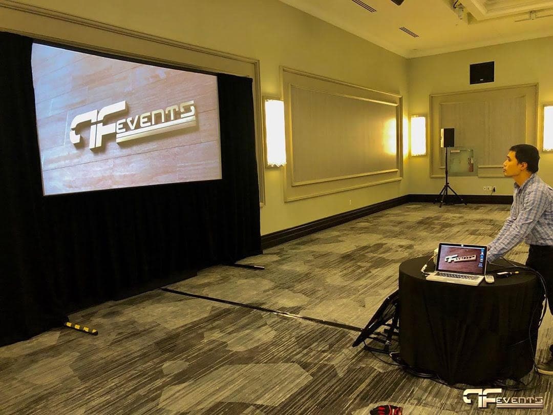 Technician testing a front-projection screen framed in black drape in a ballroom
