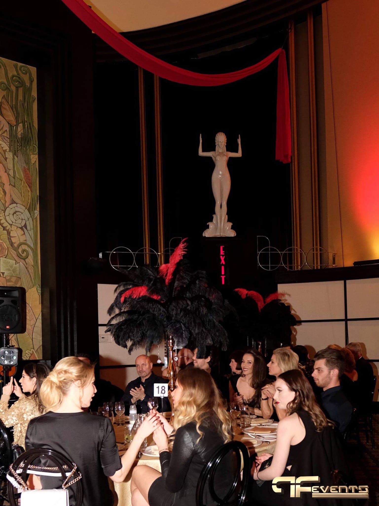 Gala tables with black and red feather centrepieces, red swag and amber uplit walls