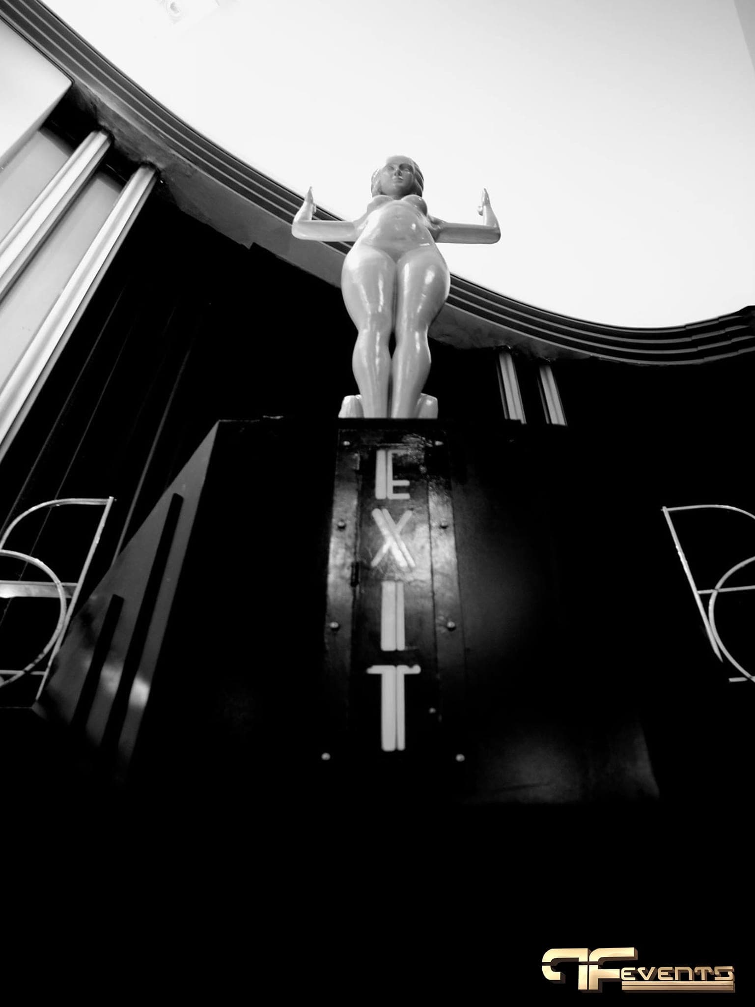 Art-deco statue above an illuminated EXIT portal inside The Eglinton Grand, black and white