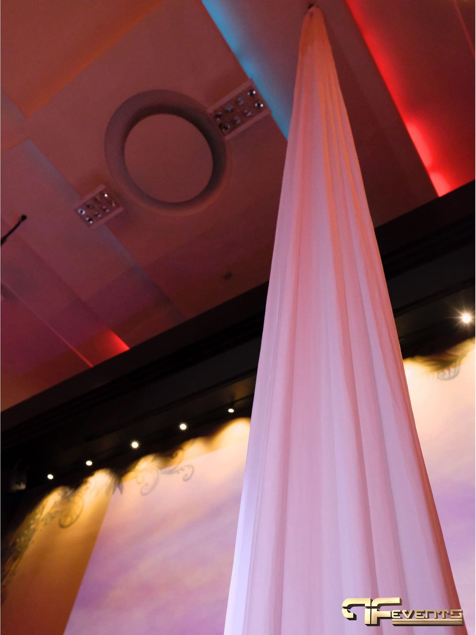 White fabric column rising to a ceiling washed in red and blue uplight