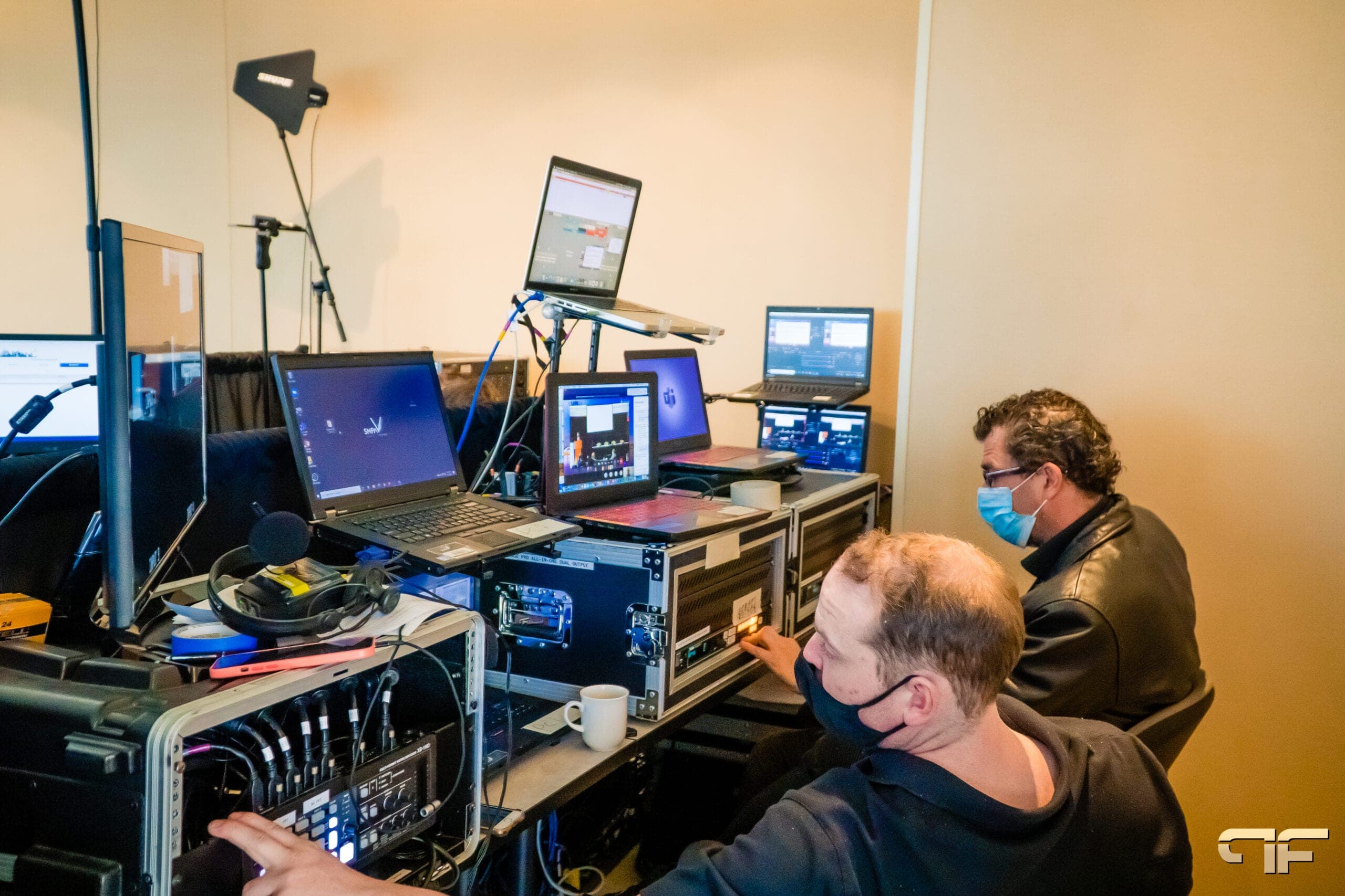 Two technicians operating rack gear and laptops at the UHN control position